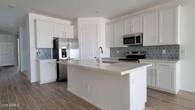 kitchen with an island with sink, appliances with stainless steel finishes, a sink, light wood finished floors, and backsplash