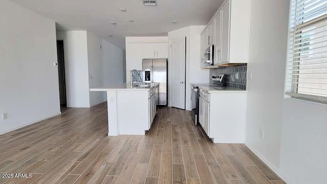 kitchen with white cabinets, light countertops, light wood-type flooring, appliances with stainless steel finishes, and a kitchen island with sink