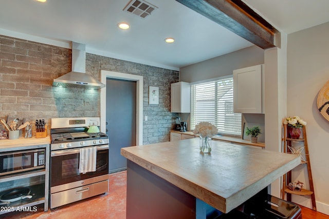 kitchen featuring wall chimney exhaust hood, a kitchen bar, stainless steel gas stove, white cabinetry, and beamed ceiling