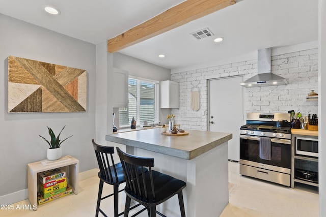 kitchen featuring a breakfast bar, white cabinetry, stainless steel appliances, wall chimney exhaust hood, and beamed ceiling