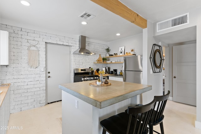 kitchen featuring appliances with stainless steel finishes, wall chimney exhaust hood, a breakfast bar, and brick wall