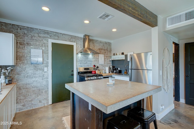 kitchen with wall chimney range hood, stainless steel appliances, a center island, and white cabinets