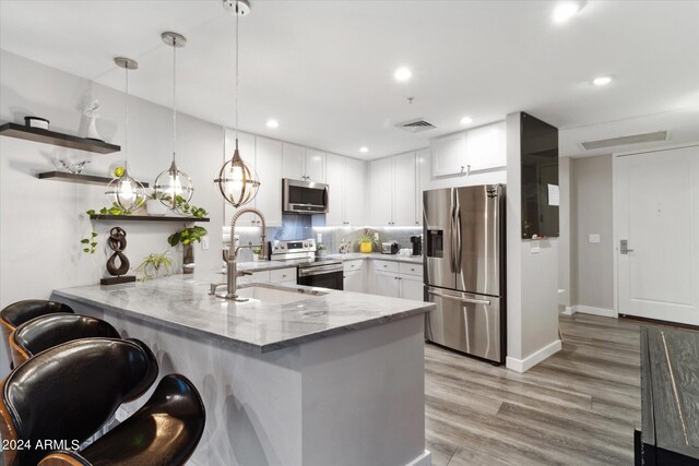 kitchen with sink, stainless steel appliances, kitchen peninsula, pendant lighting, and white cabinets