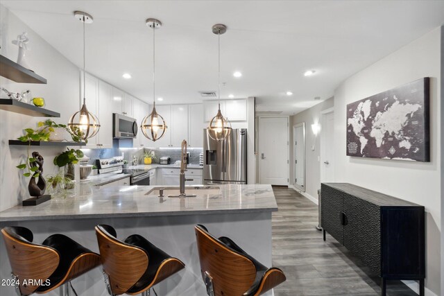 kitchen featuring kitchen peninsula, appliances with stainless steel finishes, backsplash, white cabinetry, and hanging light fixtures