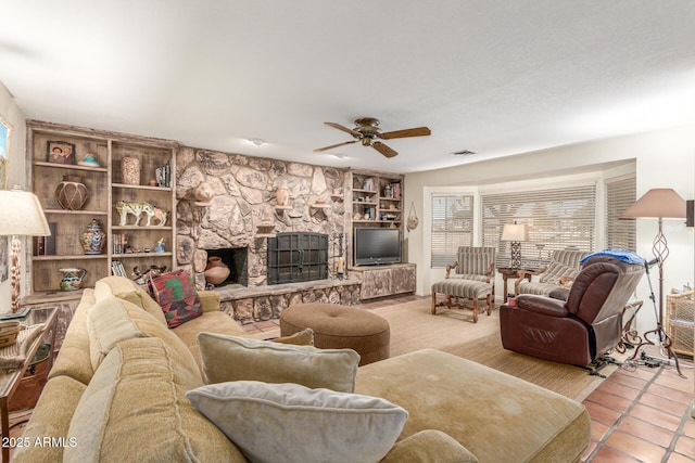 tiled living room featuring ceiling fan, a stone fireplace, and built in features