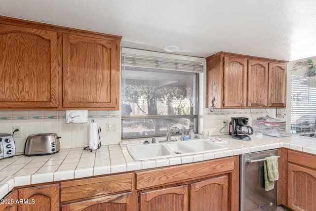 kitchen with tasteful backsplash, dishwasher, sink, and tile countertops