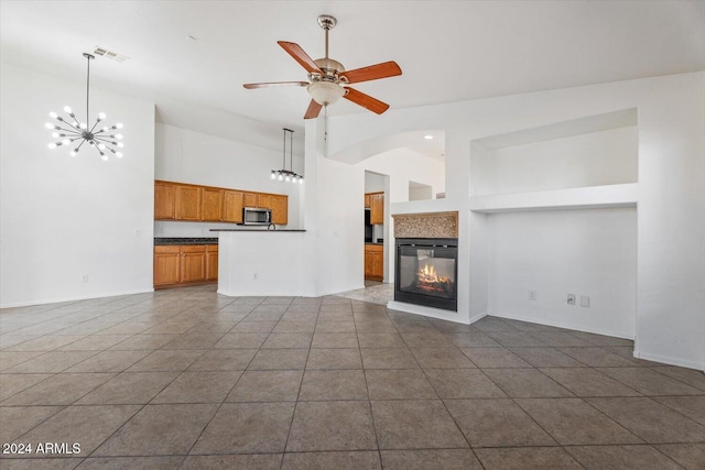 unfurnished living room with dark tile patterned floors, high vaulted ceiling, and ceiling fan with notable chandelier