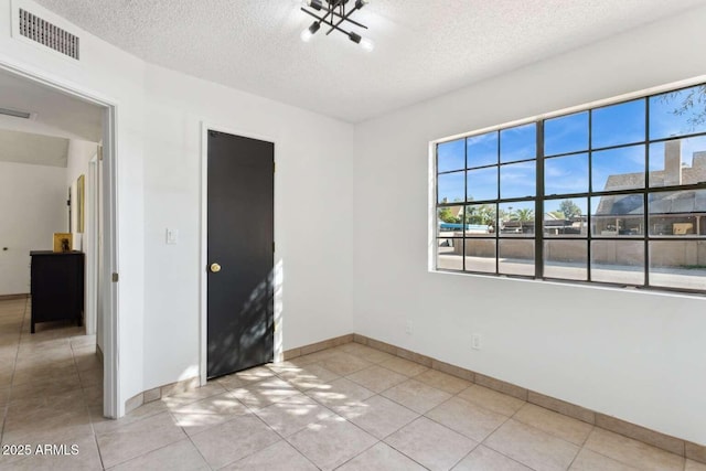 empty room featuring a textured ceiling, light tile patterned flooring, visible vents, and baseboards