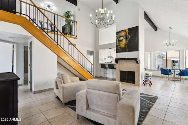 living room with light tile patterned floors, an inviting chandelier, a tile fireplace, beamed ceiling, and stairs