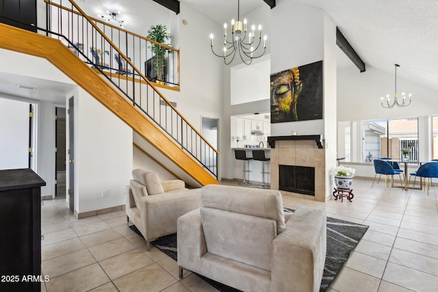 living room featuring stairs, a tile fireplace, beam ceiling, and an inviting chandelier