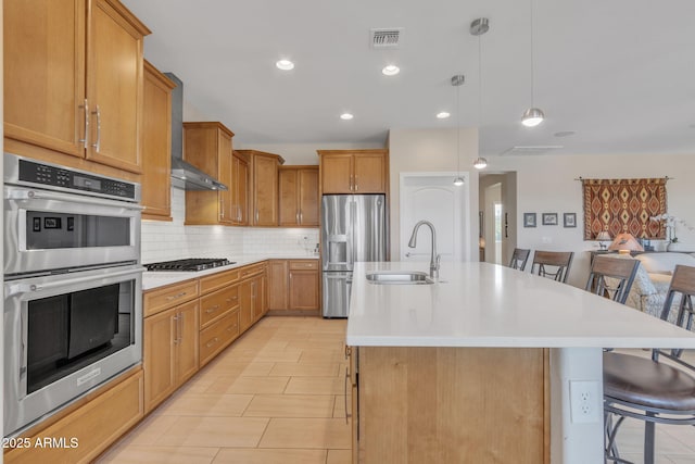 kitchen with a center island with sink, wall chimney range hood, sink, and a breakfast bar area