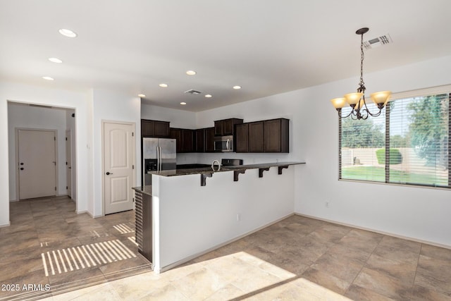 kitchen with kitchen peninsula, dark brown cabinetry, decorative light fixtures, appliances with stainless steel finishes, and a kitchen bar