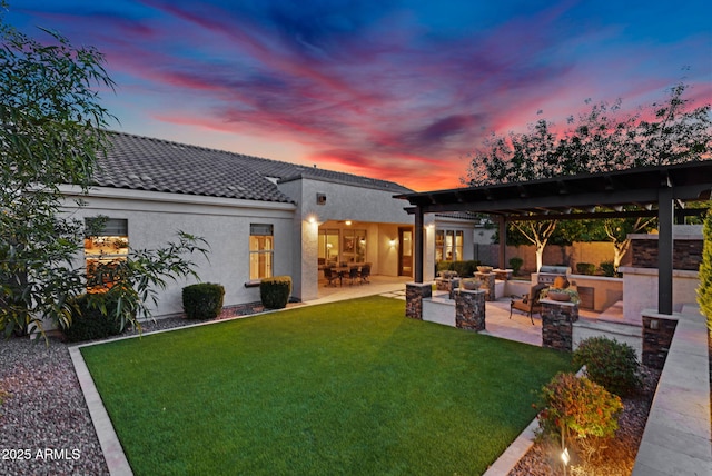 back of house at dusk with stucco siding, a tile roof, fence, a yard, and a patio area