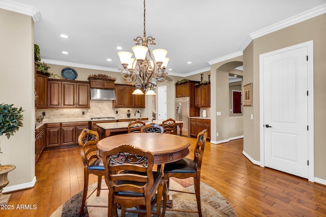 dining space with arched walkways, a chandelier, crown molding, and wood-type flooring