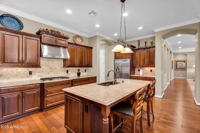 kitchen featuring visible vents, under cabinet range hood, a sink, stainless steel appliances, and arched walkways