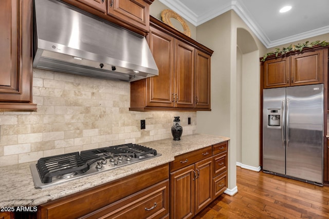 kitchen with arched walkways, ornamental molding, decorative backsplash, stainless steel appliances, and under cabinet range hood