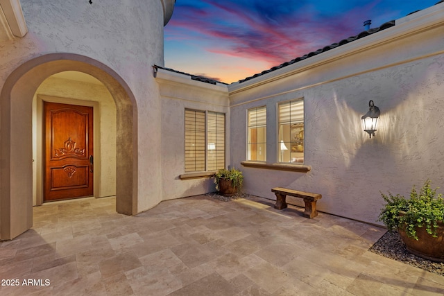 view of exterior entry with stucco siding, a patio, and a tile roof