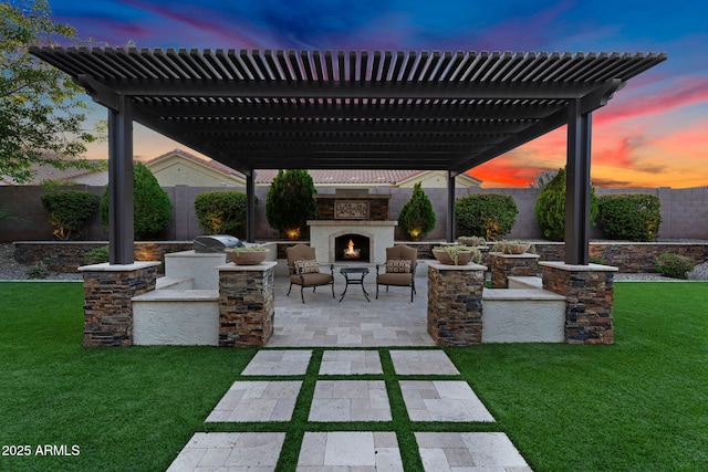 patio terrace at dusk with a yard, a pergola, an outdoor stone fireplace, and a fenced backyard