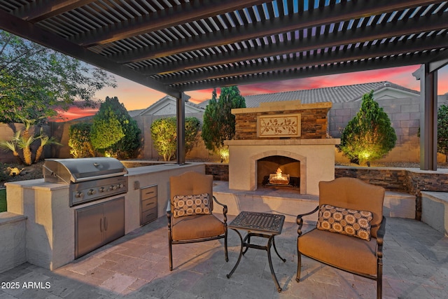 view of patio featuring area for grilling, fence, a warm lit fireplace, and grilling area