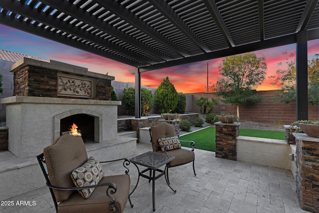 patio terrace at dusk featuring an outdoor stone fireplace, a fenced backyard, and a pergola