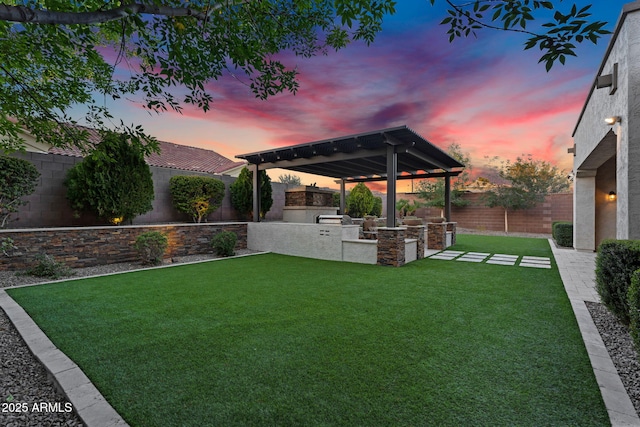 yard at dusk with an outdoor kitchen, a patio, and a fenced backyard