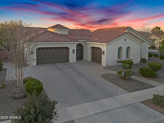 mediterranean / spanish-style home featuring a garage, stucco siding, driveway, and a tiled roof