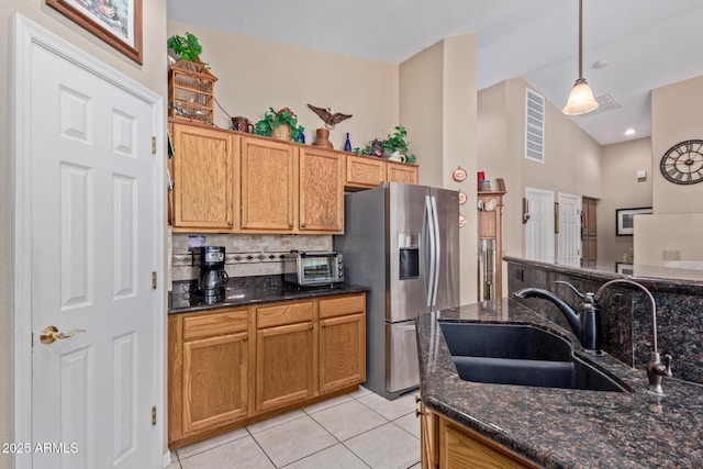 kitchen featuring stainless steel refrigerator with ice dispenser, dark stone countertops, decorative backsplash, sink, and hanging light fixtures