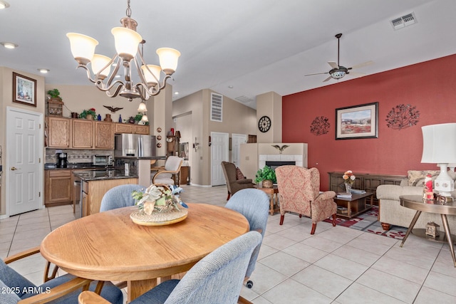 tiled dining area featuring ceiling fan with notable chandelier, a tile fireplace, and vaulted ceiling