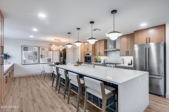 kitchen featuring visible vents, a kitchen breakfast bar, wall chimney exhaust hood, light wood-style flooring, and appliances with stainless steel finishes