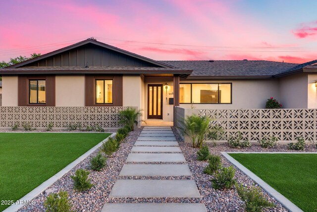 view of front of home with a shingled roof, stucco siding, and a front lawn