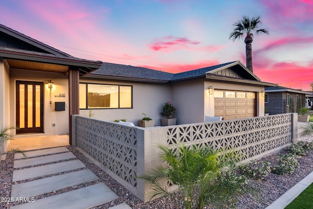 ranch-style house with stucco siding, a fenced front yard, a shingled roof, and a garage