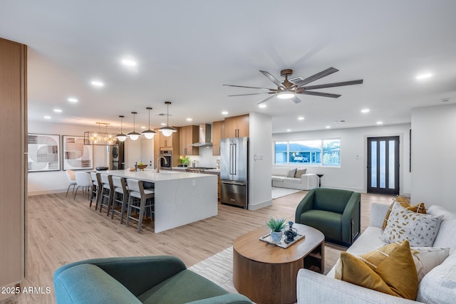 living room featuring recessed lighting, baseboards, ceiling fan with notable chandelier, and light wood-style floors