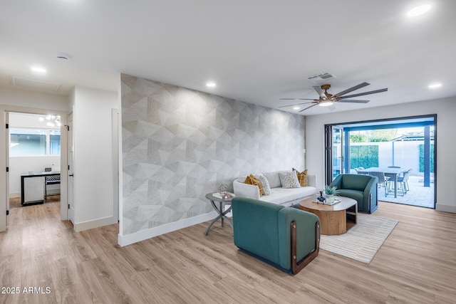 living area with visible vents, an accent wall, baseboards, light wood-style floors, and ceiling fan