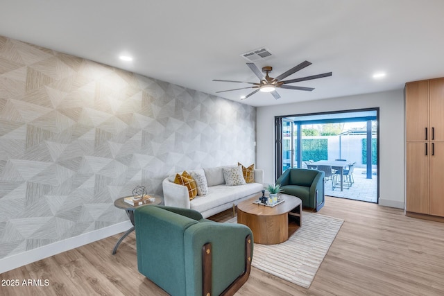 living area with baseboards, a ceiling fan, light wood finished floors, and visible vents