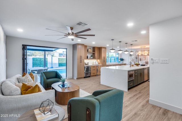 living room with a ceiling fan, baseboards, visible vents, and light wood-style flooring