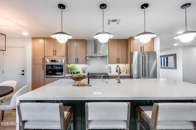 kitchen featuring visible vents, light countertops, a sink, stainless steel appliances, and wall chimney exhaust hood