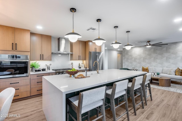 kitchen featuring appliances with stainless steel finishes, a breakfast bar area, light countertops, wall chimney exhaust hood, and visible vents