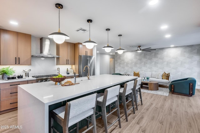 kitchen with wall chimney range hood, stainless steel appliances, a ceiling fan, wallpapered walls, and visible vents