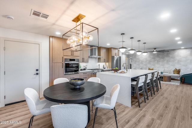 dining room featuring light wood-style flooring, ceiling fan with notable chandelier, recessed lighting, wallpapered walls, and visible vents