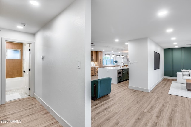 corridor featuring light wood-style floors, a sink, baseboards, and recessed lighting