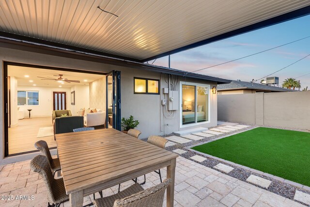 back of house at dusk with fence, a patio, outdoor dining area, stucco siding, and a yard