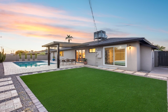 back of property at dusk with a patio, a fenced backyard, stucco siding, a fenced in pool, and a yard