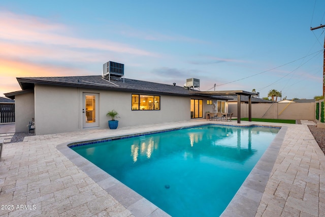 pool at dusk with a patio, a fenced in pool, and central AC unit