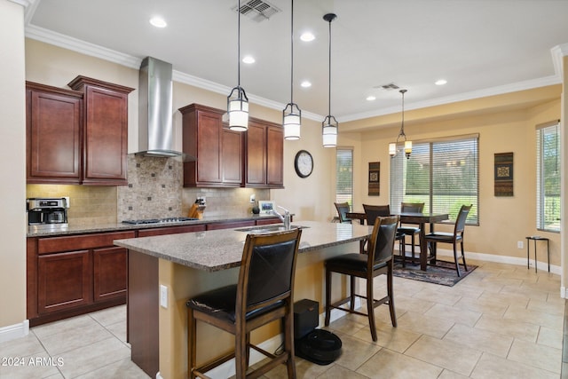 kitchen with wall chimney exhaust hood, a kitchen bar, a center island with sink, and decorative light fixtures