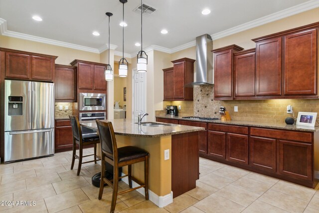 kitchen featuring wall chimney exhaust hood, pendant lighting, an island with sink, crown molding, and stainless steel appliances