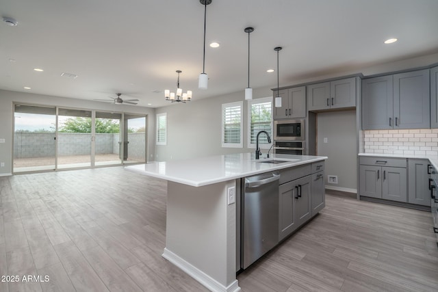 kitchen featuring pendant lighting, sink, dishwasher, a center island with sink, and built in microwave