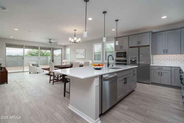 kitchen with a kitchen island with sink, sink, gray cabinets, and stainless steel appliances