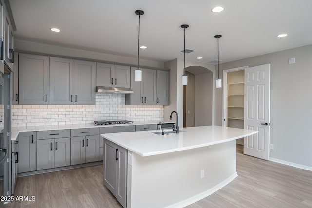 kitchen featuring decorative light fixtures, sink, stainless steel gas cooktop, a center island with sink, and light hardwood / wood-style flooring