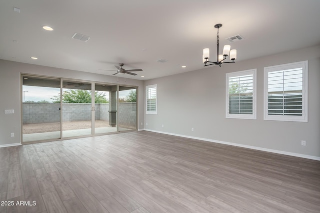 empty room with plenty of natural light, ceiling fan with notable chandelier, and light hardwood / wood-style floors