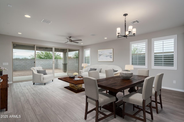 dining space with ceiling fan with notable chandelier and light hardwood / wood-style floors